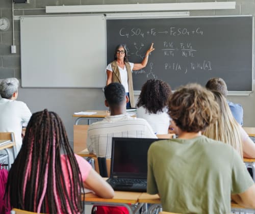 math teacher giving a lesson in front of a chalk board to a room full of students