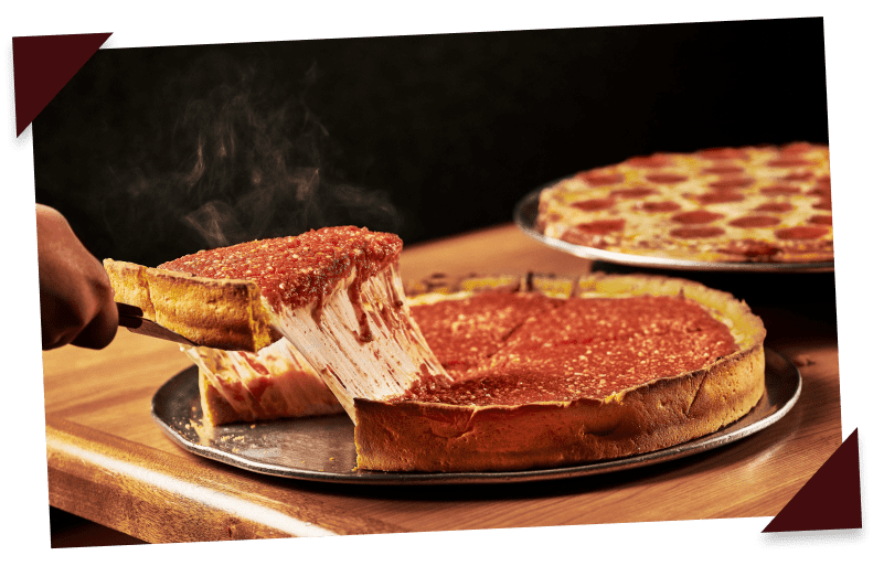 A steamy slice of deep-dish pizza from Beggars Pizza is lifted with a pie server. A pepperoni pizza sits in the background.