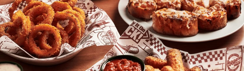 A spread of Beggars Pizza onion rings, mozzarella sticks and marinara sauce, and tomato bread