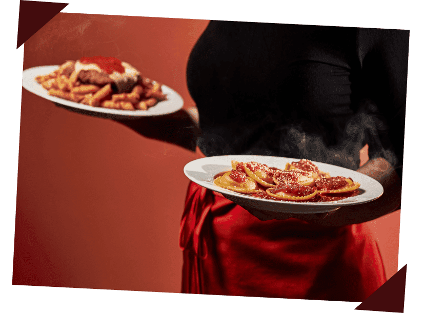 A close-up of a Beggars Pizza server wearing a red apron and carrying a plate of chicken parmesan and a plate of ravioli