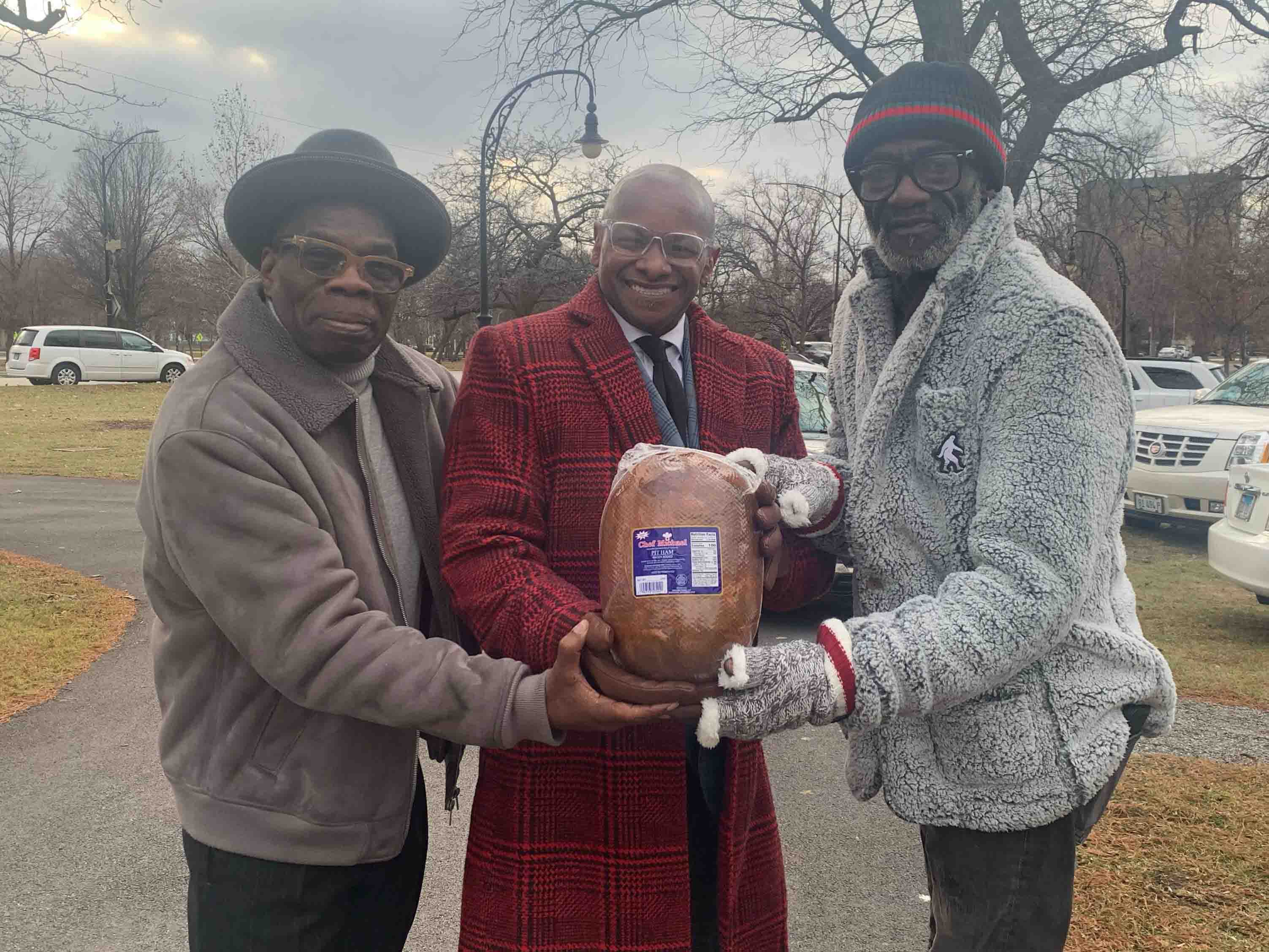 3 people holding up a ham standing outdoors