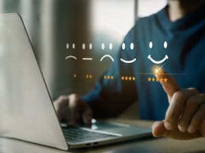 A person sitting at a desk with a laptop in front. Floating on the image is a scale of smiley faces ranging from a frowny face to a happy face with corresponding star ratings underneath ranging from 1 to 5