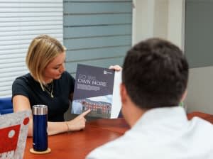 A blonde woman points to a marketing booklet in a conference room