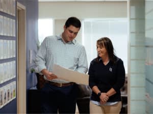 Two people in business casual clothing looking at a piece of paper in an office hallway