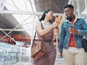 Two young people smiling and sharing a moment on a smartphone in a shopping center