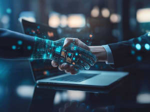 A human shaking the hand of a robot with a laptop in the background 