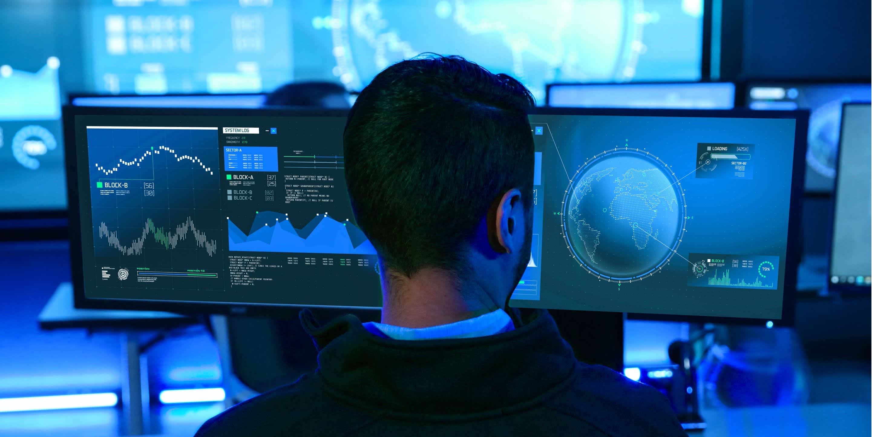 Man at a computer looking at blue charts and global maps | DOT Cybersecurity Services