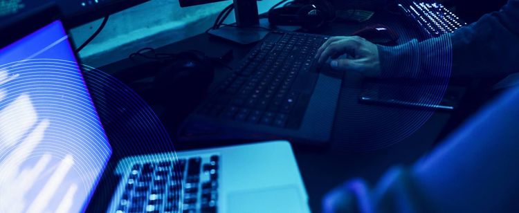 Blue tinted image of a person’s hands on a laptop and external keyboard | cybersecurity risk audit