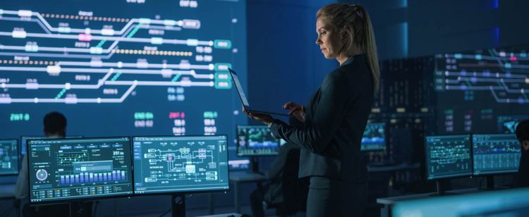 7 Cybersecurity Trends In 2021 | Woman in a security operations center, holding a laptop surrounded by monitors