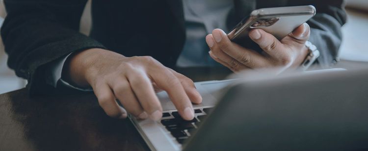 A businessman holds a mobile device and types on a laptop | The Difference Between Edge Security and Endpoint Protection | DOT Security