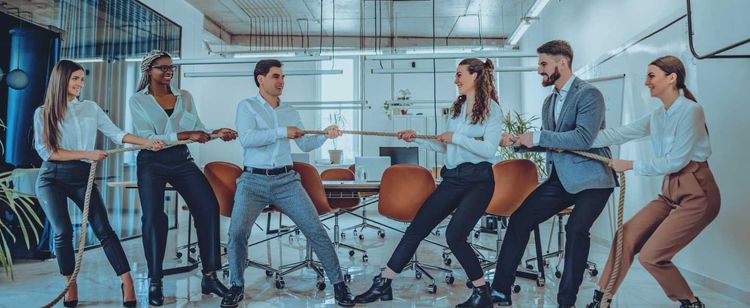 People in business casual attire playing tug of war in an office