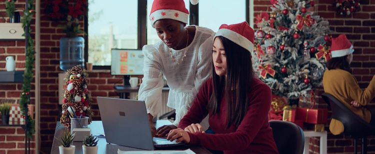 two workers on laptop with holiday hats on | 5 ways to promote employee cybersecurity during the holidays