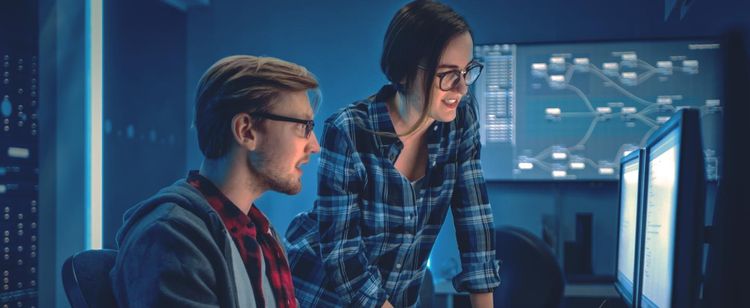 Two Cyber Developers looks over code on a desktop. | A Day in the Life | DOT Security