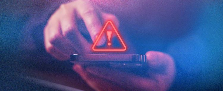 Triangle warning sign over a smartphone in someone's hands.