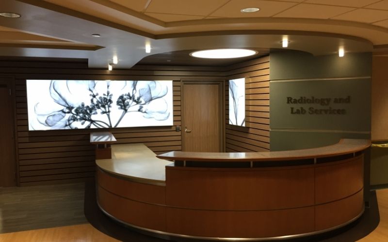 Front desk inside the hospital with ceiling lights, a big screen and the words 'Radiology and Lab Services' on the wall.