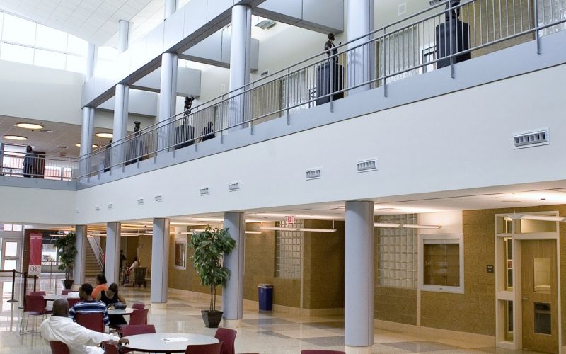 Two-story hallways with bright linear pendant lights and four students sitting at tables nearby.