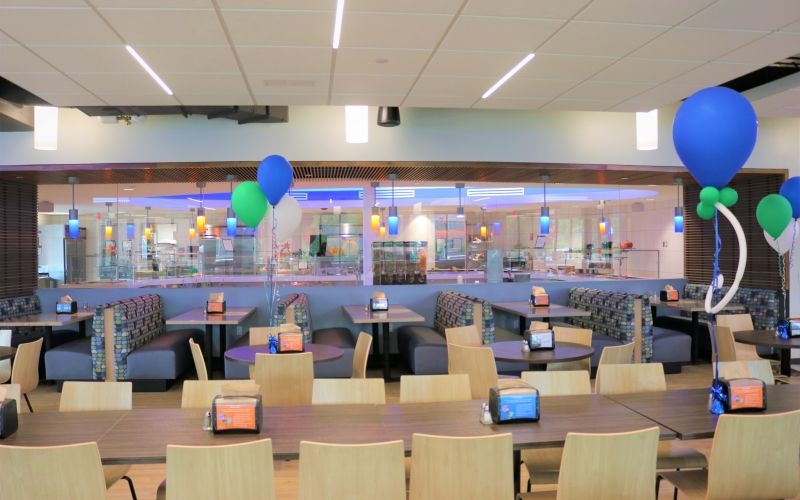 Another view of the dining hall with a long, wood table, more seating and decorated with balloons.