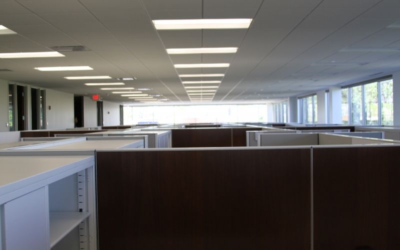 Various cubicles inside a room with many ceiling lights.