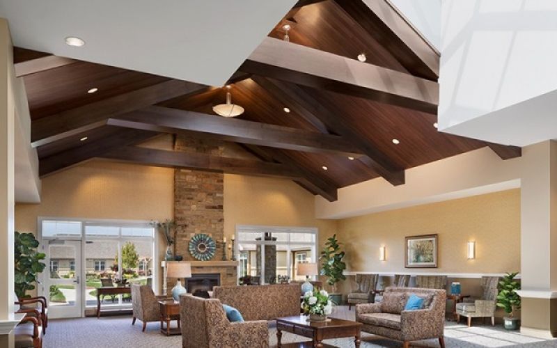 A different view of the living room at Silverado Assisted Living with comfortable couches, carpet, ceiling lights and large wood beams.