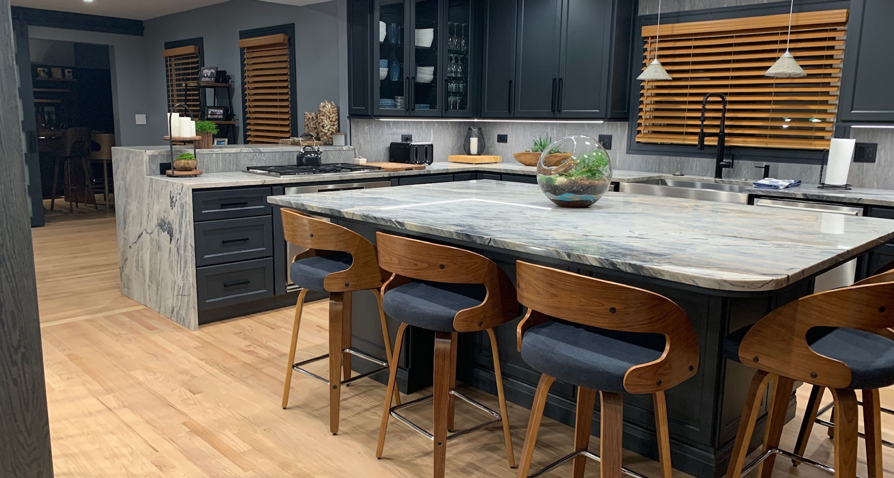 Kitchen with custom stonework countertops and island with black cabinets and wooden barstools