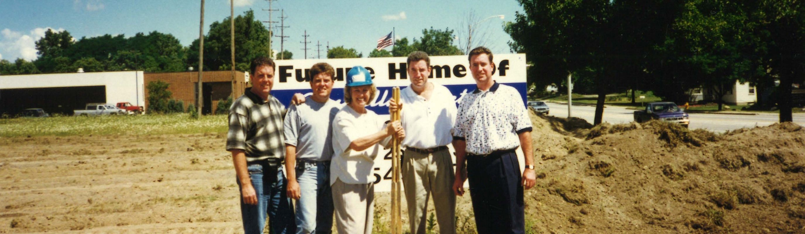 Five members of the Connelly family standing next to each other and smiling on top of a patch of land that will be the future home of Connelly Electric.