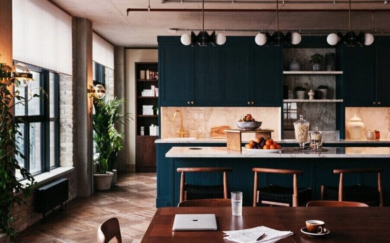 A view of the kitchen showing some cabinets, a countertop, a table and chairs, as well as a large window with natural light.