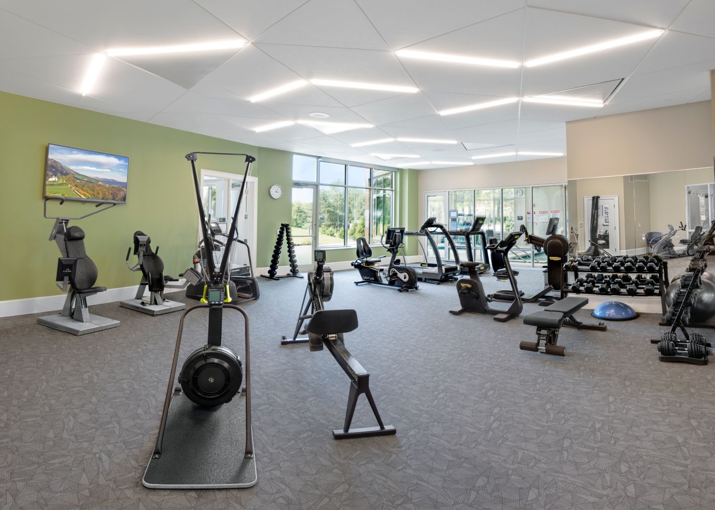 Large fitness center with linear lights, two treadmills, weights, a television and other exercise machines.