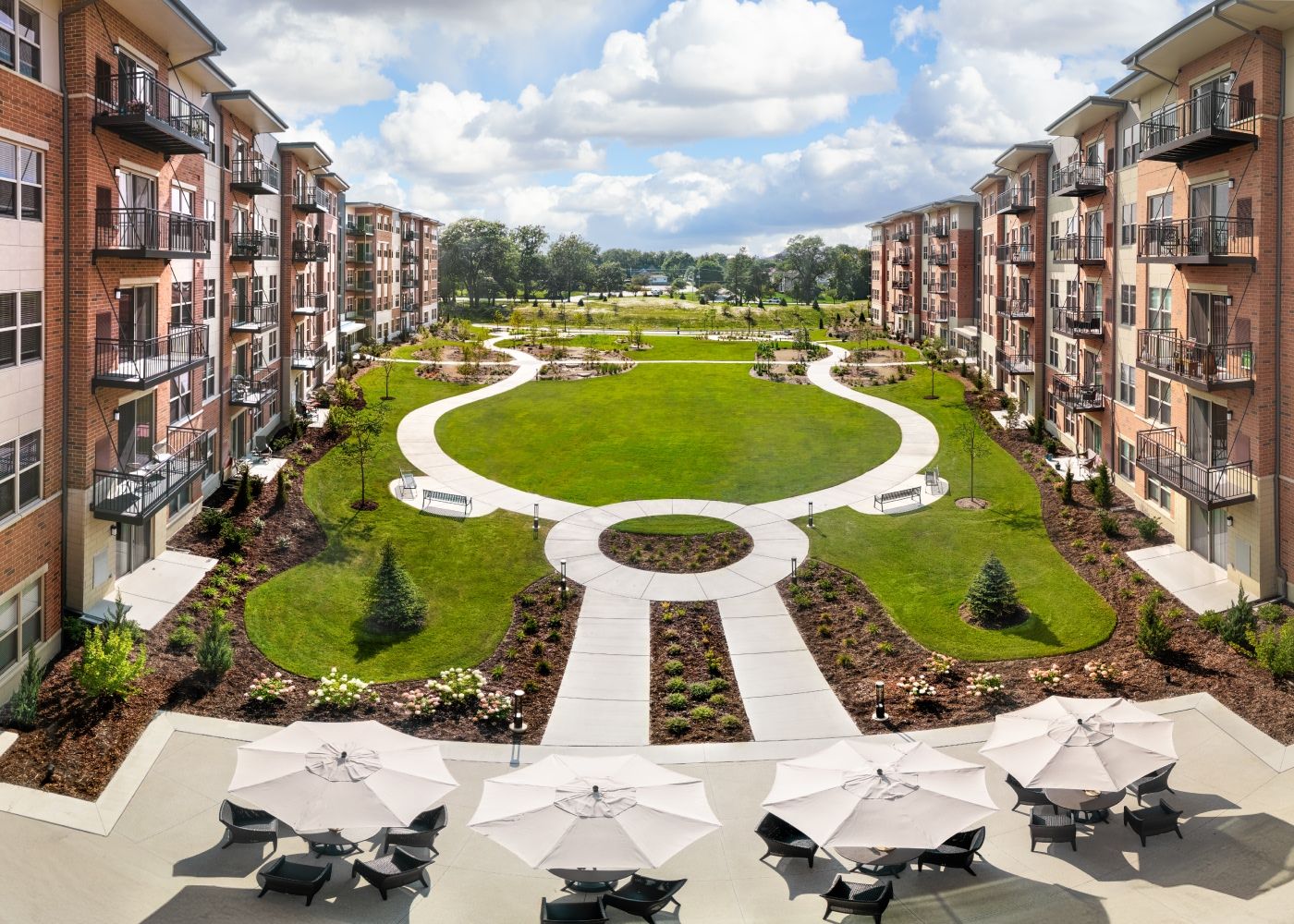 Outside view of the property with green fields, flowers and outdoor tables, chairs and umbrellas.