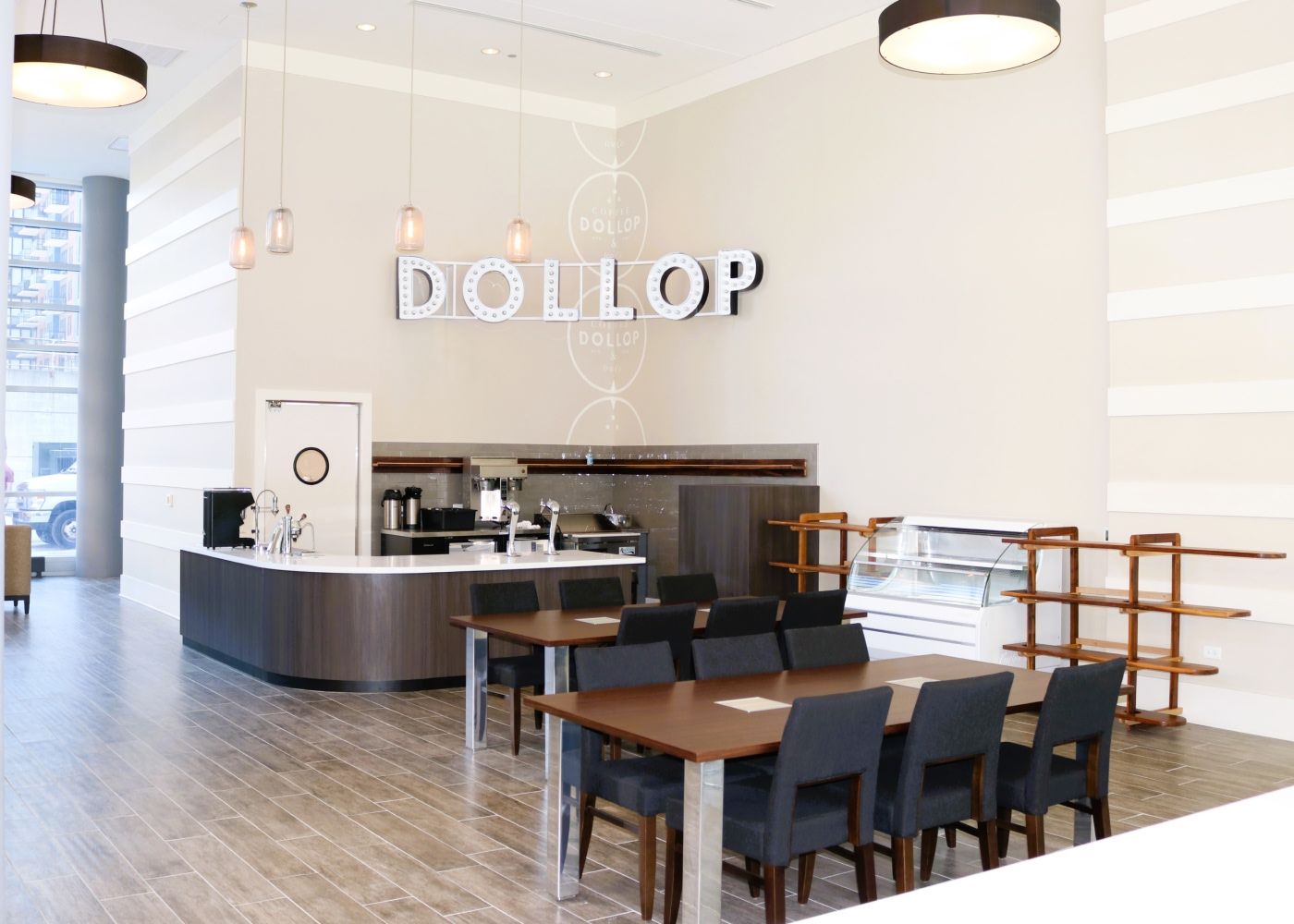 A coffee area with couple tables, chairs and a sign that says "Dollop" on the wall.