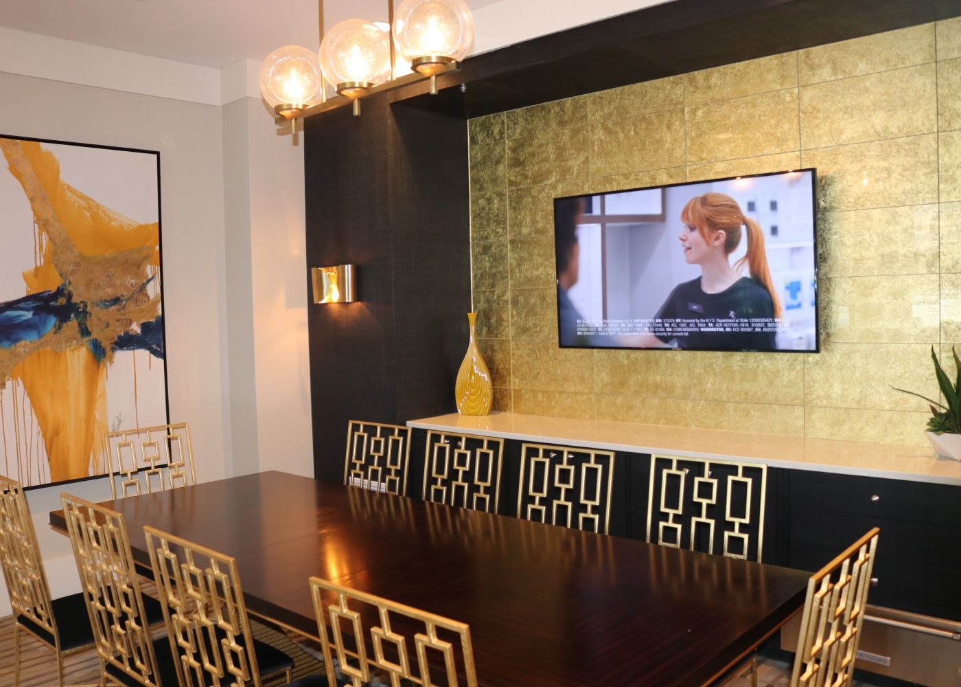 A meeting room at Alta Roosevelt with a large wooden table, chairs and a television currently playing a show.