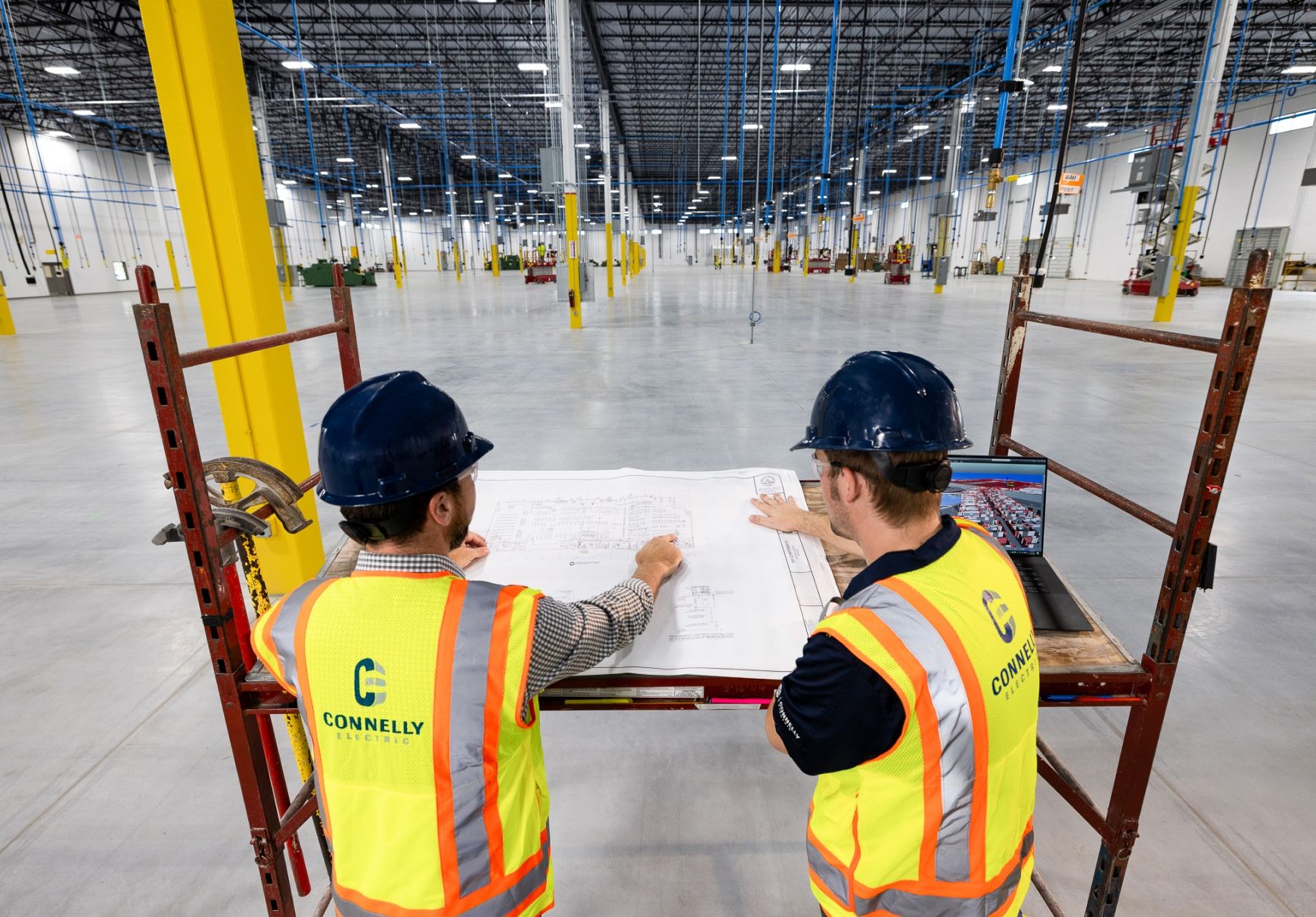 Two Connelly Electric engineers reviewing blueprint of electric systems in a large open warehouse.