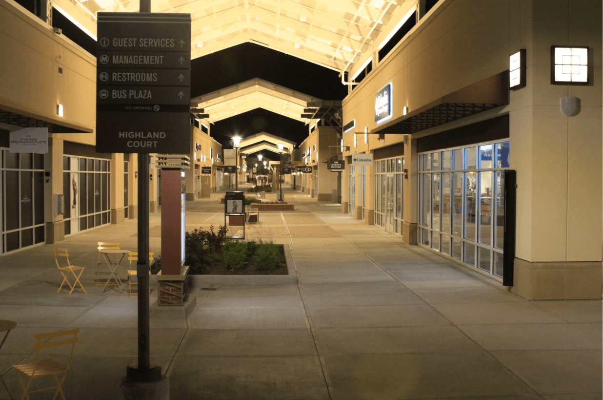 Long outside passageway showing street signs, glass windows and store signs illuminated at night.