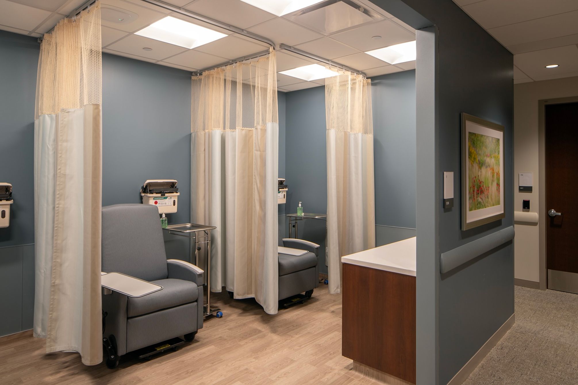 Room with two sofa chairs and medical waste dispensers with curtains between them.