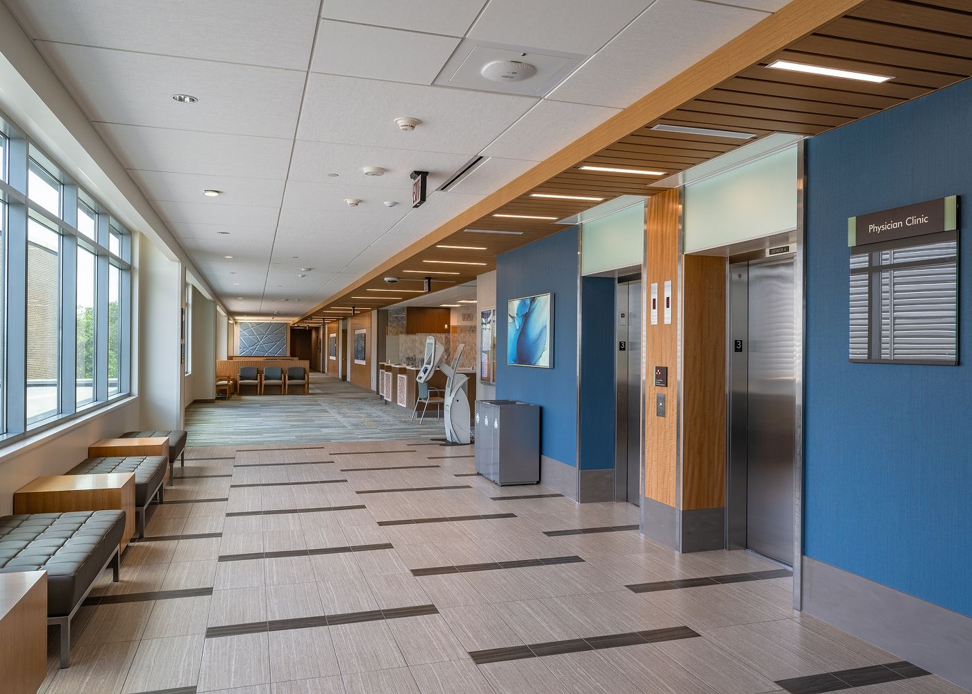 A long hallway on the ground-level showing some seating and two elevators.
