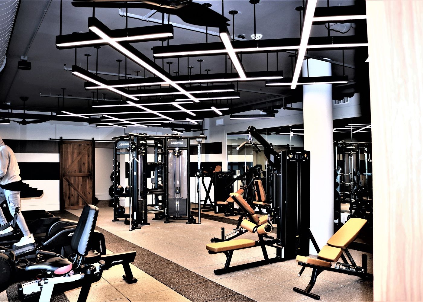 The gym facilities with a couple exercise machines and linear pendant lights.
