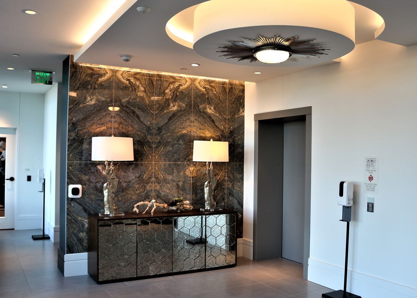 Hallway with a large light piece, marble walls and table lamps.