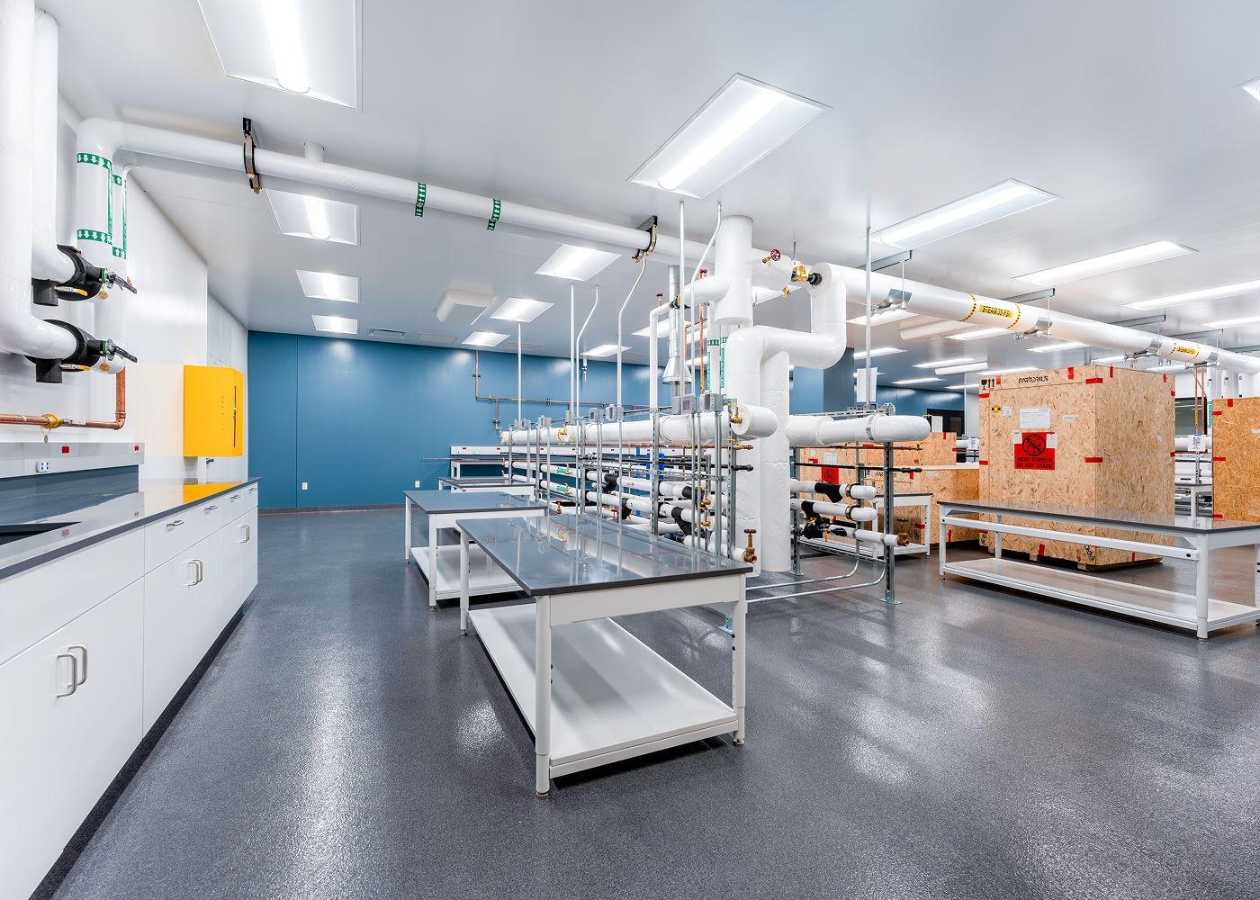 Large lab with various long tables, large shipment wood boxes and lab plumbing systems. 