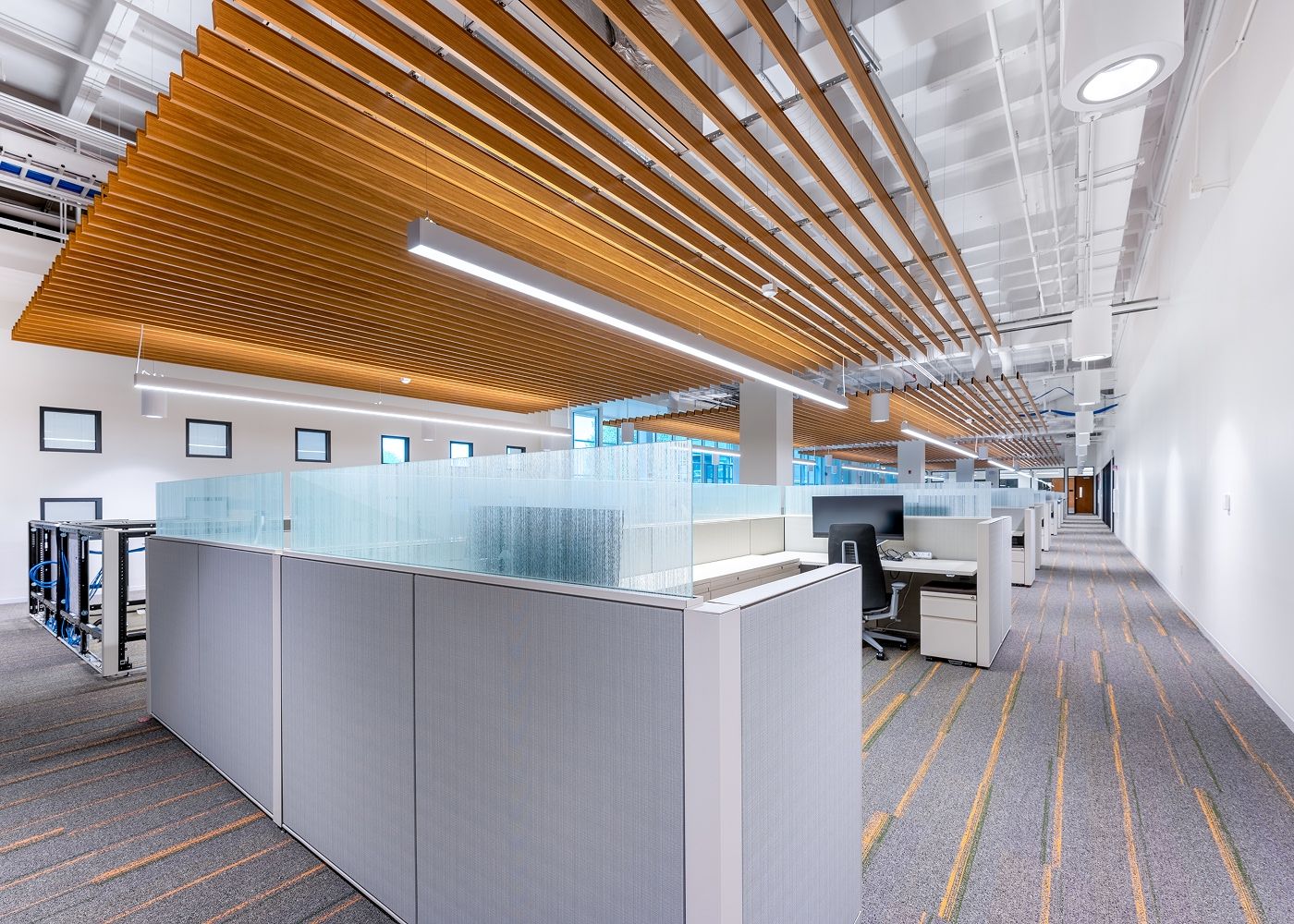 Large room with bright lit cubicles, office equipment and linear lights.