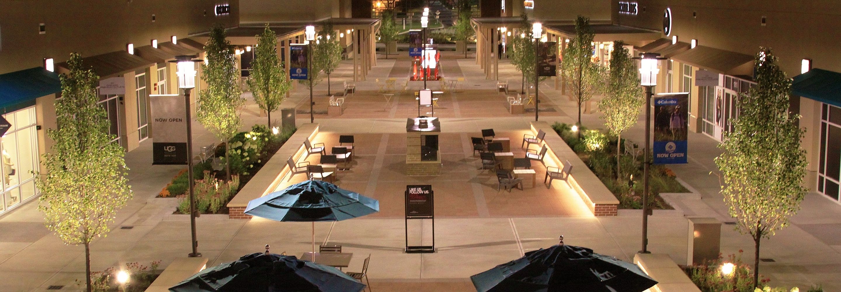 Outdoor outlets area with decorative lighting, scones and poles illuminated at night.