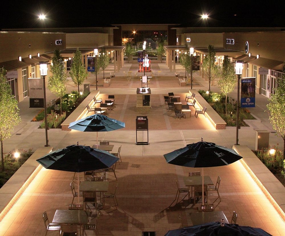 Outdoor outlets area with decorative lighting, scones and poles illuminated at night.