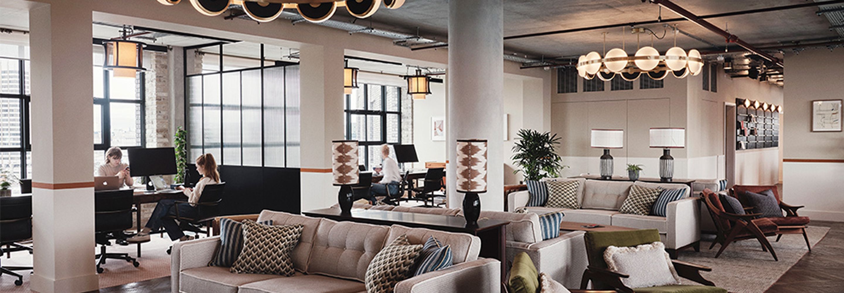 Co-working space with a couple gray couches, tables and natural light coming in from large windows.