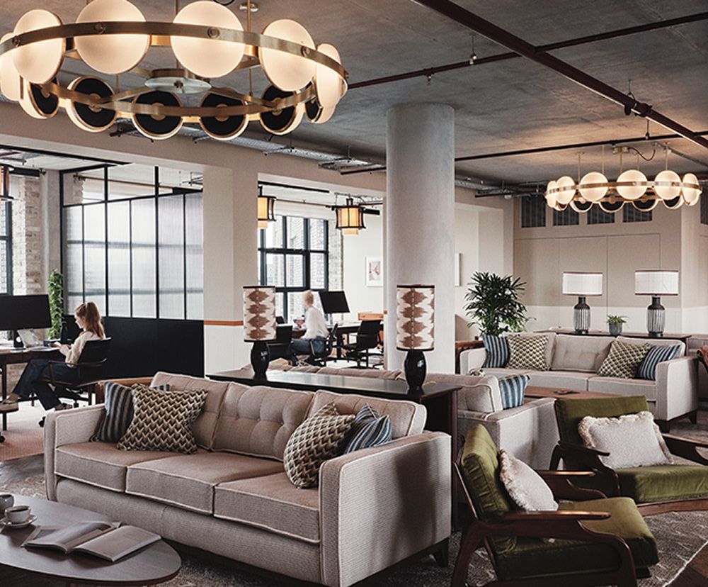 Co-working space with a couple gray couches, tables and natural light coming in from large windows.
