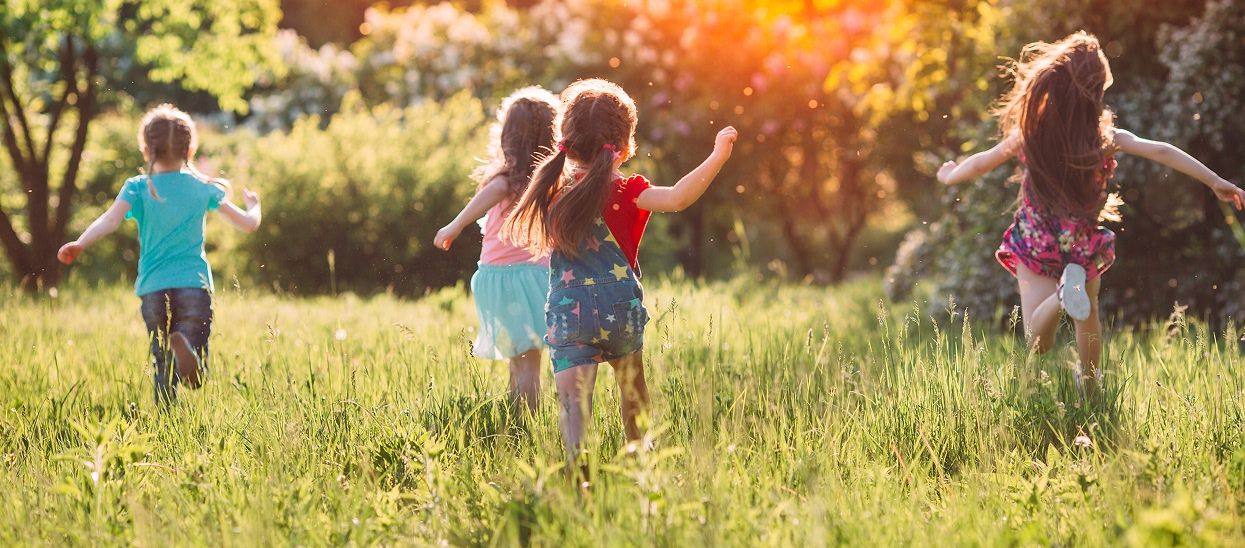 Children frolic through a meadow toward the setting sun and away from the camera