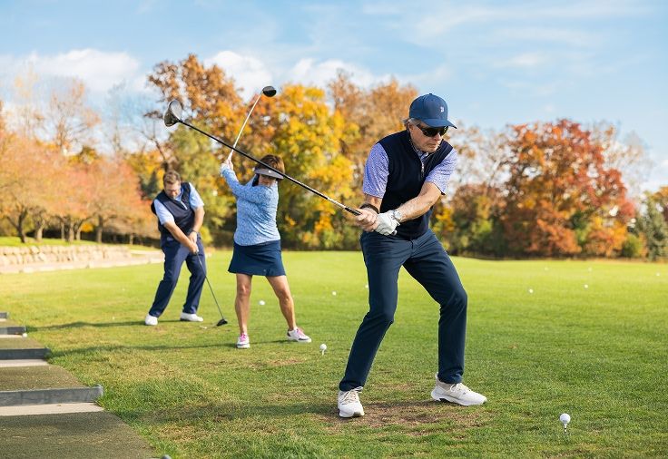 three people teeing off at a driving range