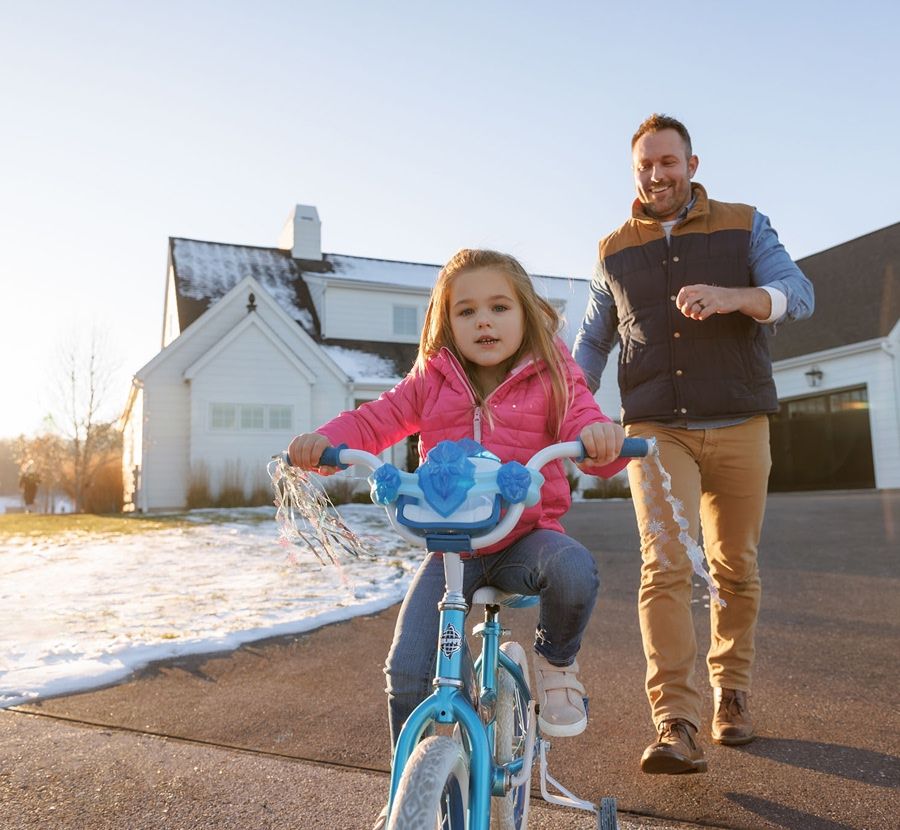 A dad teaching his daughter how to ride a bike outside their house