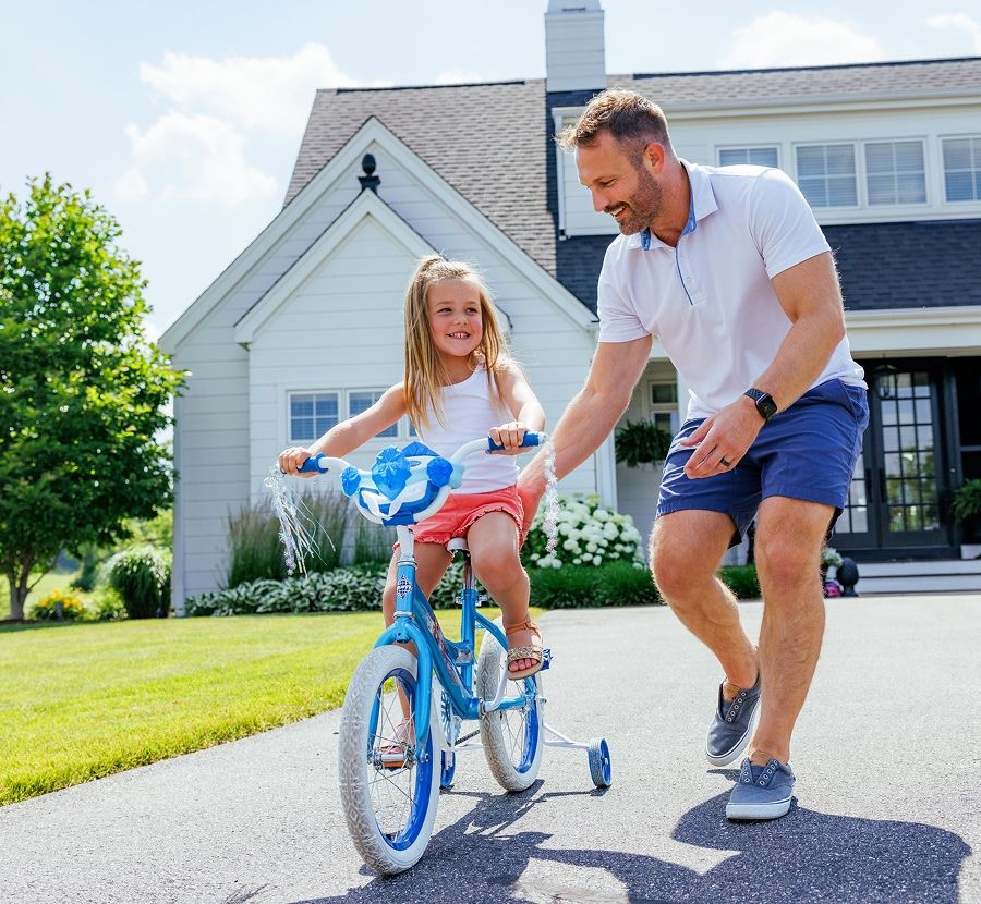 A dad teaching his daughter how to ride a bike on their driveway