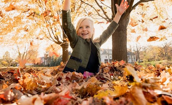young girl playing in leaves during autumn