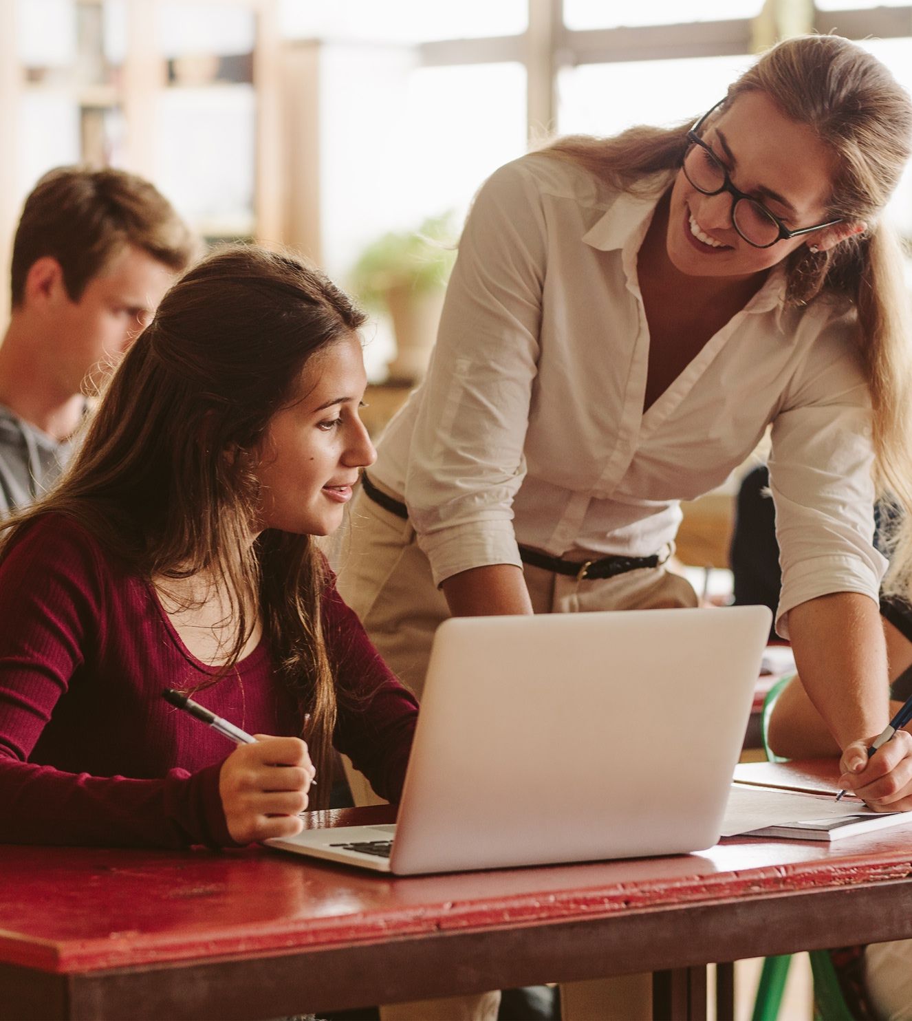 teacher leaning over a students desk to help in a classroom