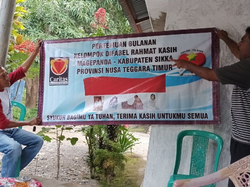 Two people hold up a sign advertising monthly meetings for a group for persons with disability