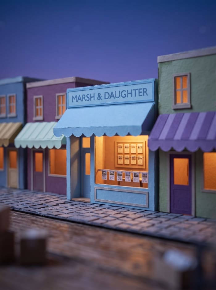 A model estate agent with a blue awning and property cards in the window.